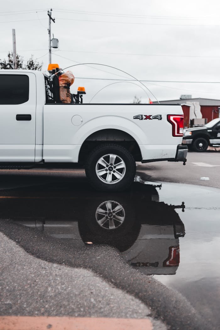 A white pickup truck, with visible reflections in a puddle, captured outdoors.